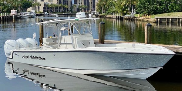 Sleek white motorboat named 'Reel Addiction' docked in calm marina waters.
