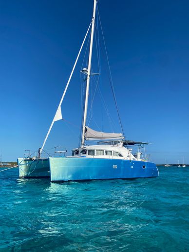 Blue catamaran sailing on clear turquoise water.