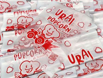 Packets of Urai Popcorn with red branding and cartoon popcorn character.