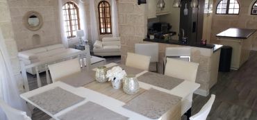 Bright dining and living area with white furniture and stone walls.