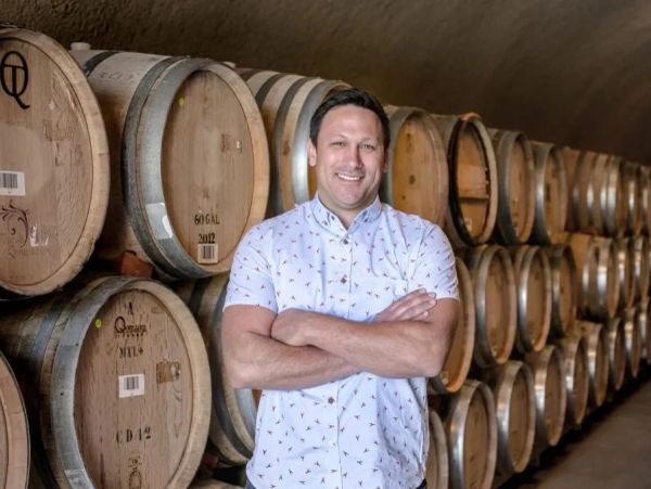 Man stands confidently in a wine cellar with barrels.