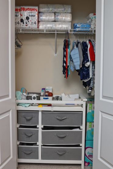 Organized baby closet with diapers, clothes, and storage bins.