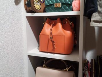 A white shelf holding three stylish handbags in different colors and designs.