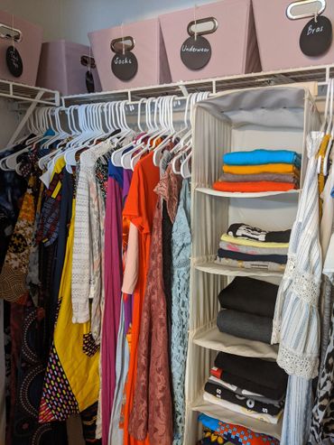 Organized closet with clothes on hangers and labeled storage bins above.