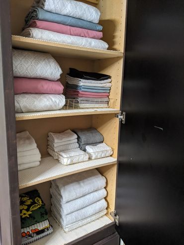 Organized cabinet shelves with neatly folded towels and bedsheets in various colors.