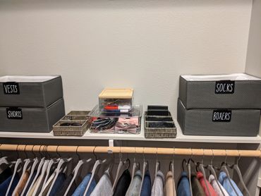 Organized closet shelf with labeled bins and hanging clothes below.