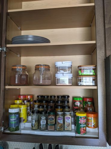 Organized kitchen cabinet with spices, jars, and plates.