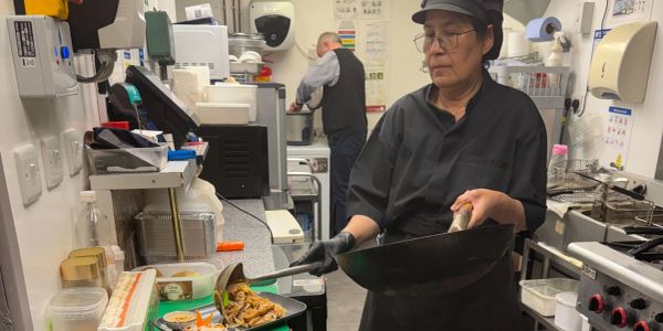 Aoy, our Chef plating stir-fried noodles in a kitchen.