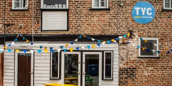 Exterior of a brick building decorated with blue, white, and yellow bunting for a youth club.