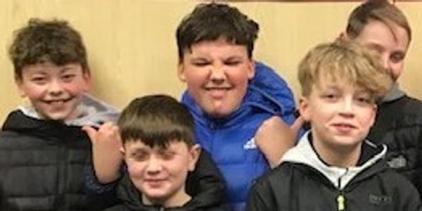 A group of five boys smiling indoors, dressed in casual jackets.