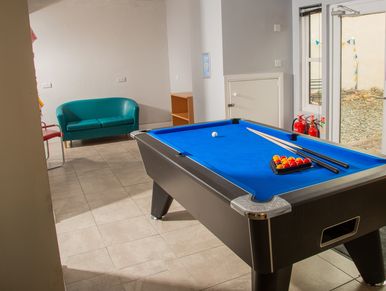 A blue pool table with cues and balls in a bright room with seating.