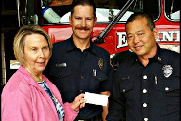 Photo of a member giving a check t the firemen of Walnut's Fire Station #61 to purchase a new clothe