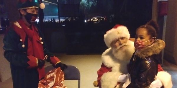 Image of Santa listening to child's wish list and Santa's helper elf nearby with a candy cane at the