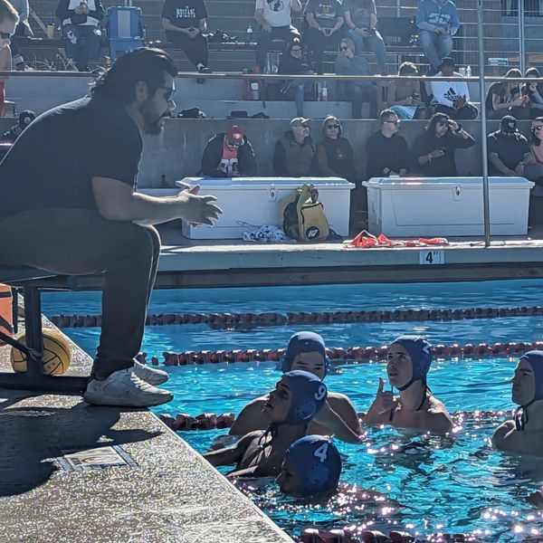 Coach talks to water polo players in the pool during a game.