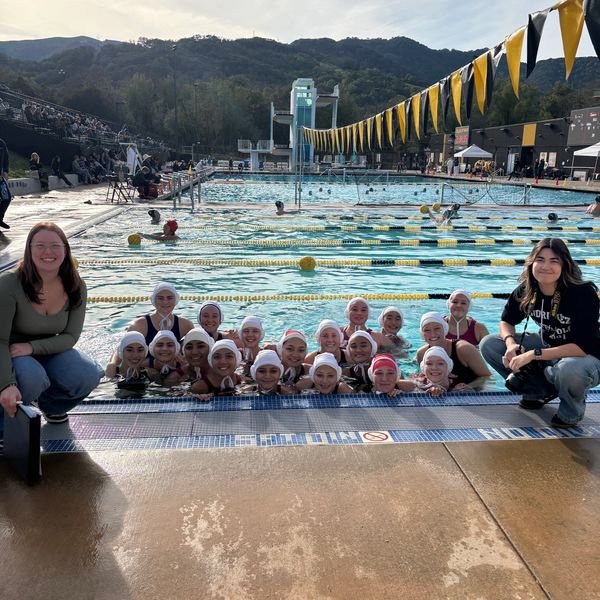 Water polo team posing at the pool edge with two coaches nearby.