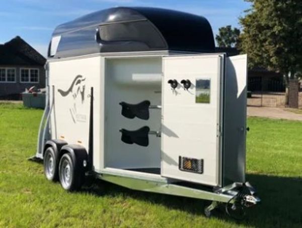 A white two-wheeled horse trailer with an open door on grass.