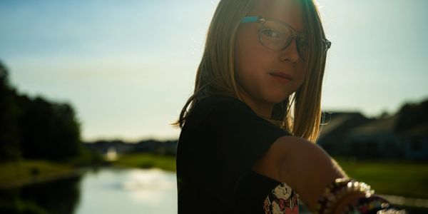 Girl wearing glasses reaching out with a scenic sunset background.