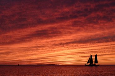 Firey skies with sailboat silhouette on the horizon