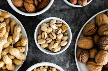 Various nuts in bowls on a dark surface.