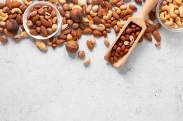 Various nuts in bowls and a wooden scoop on a gray background.