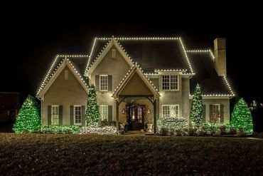A house beautifully decorated with white and green Christmas lights at night.