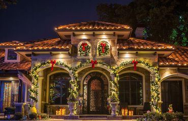 A beautifully decorated house with Christmas lights and wreaths at night.