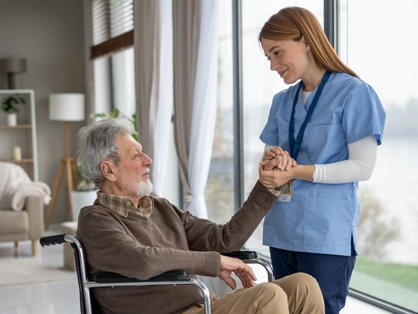 An elderly man smiles at his caregiver in a bright and airy room.