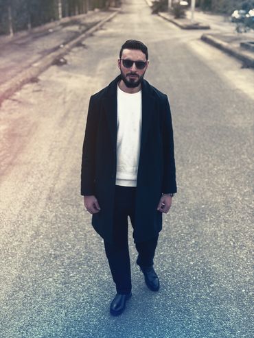 Man in black coat and sunglasses walking on an empty street.