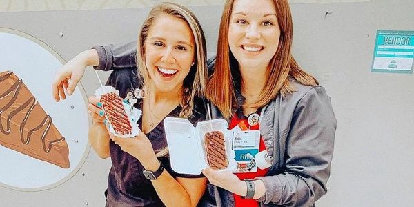 Two smiling women in scrubs holding chocolate desserts outside a dessert truck.