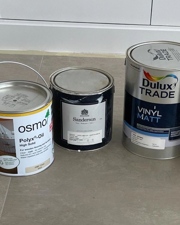 Three paint cans of different brands on a tiled floor.
