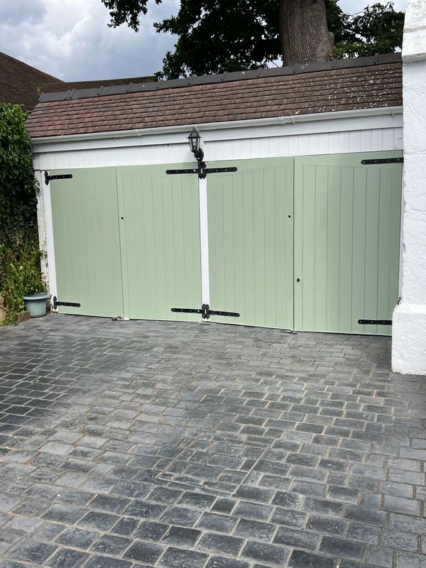 Green garage doors with black hinges on a stone driveway.