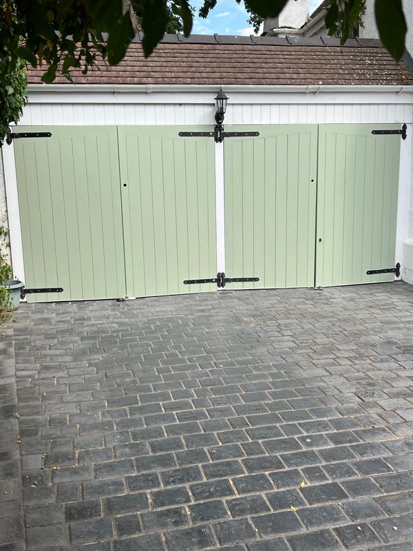 A green double garage door with black hinges and a gray brick driveway.