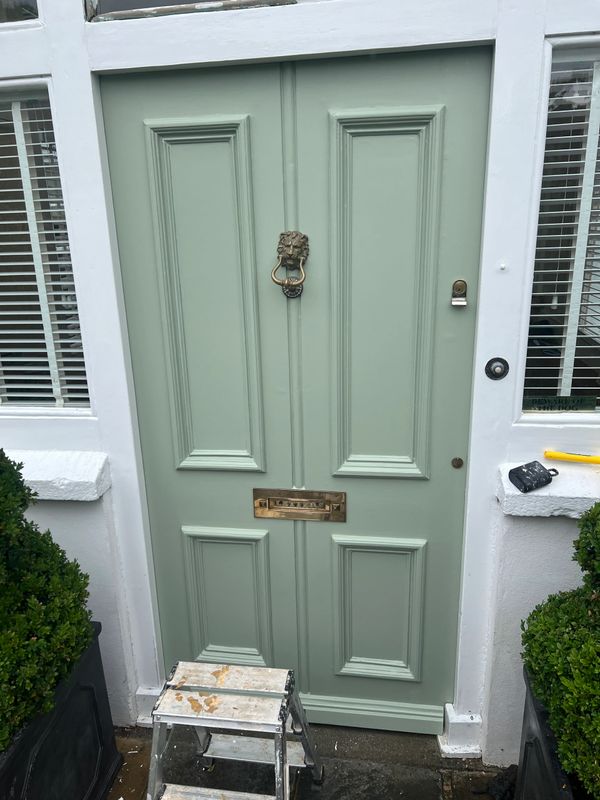 Green front door with lion head knocker and mail slot, surrounded by white frame.