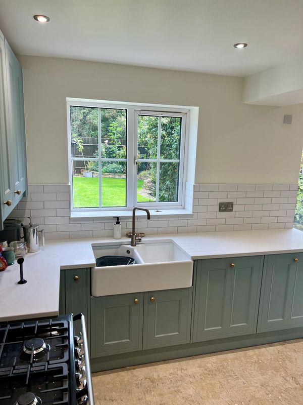 Modern kitchen with green cabinets and a large window overlooking a garden.