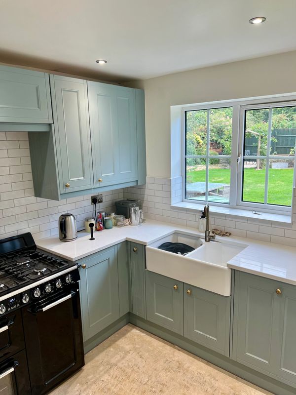 Modern kitchen with mint green cabinets and a large window overlooking a garden.