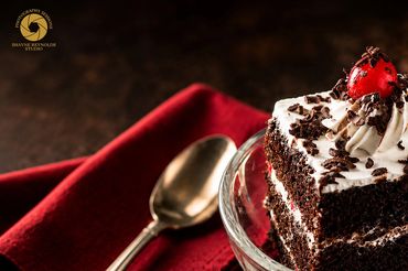 Chocolate cake slice with cream, chocolate shavings, and a cherry on top.