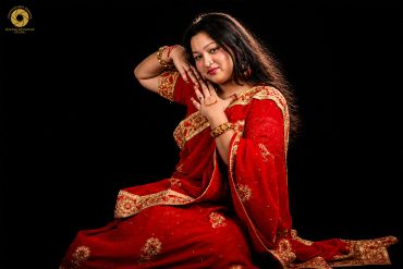 Woman in a traditional red and gold saree posing gracefully against a black background.