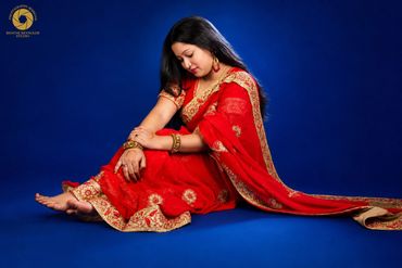 Woman in a red traditional saree sitting gracefully against a blue backdrop.