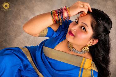 A woman dressed in a blue saree with colorful bangles poses gracefully.