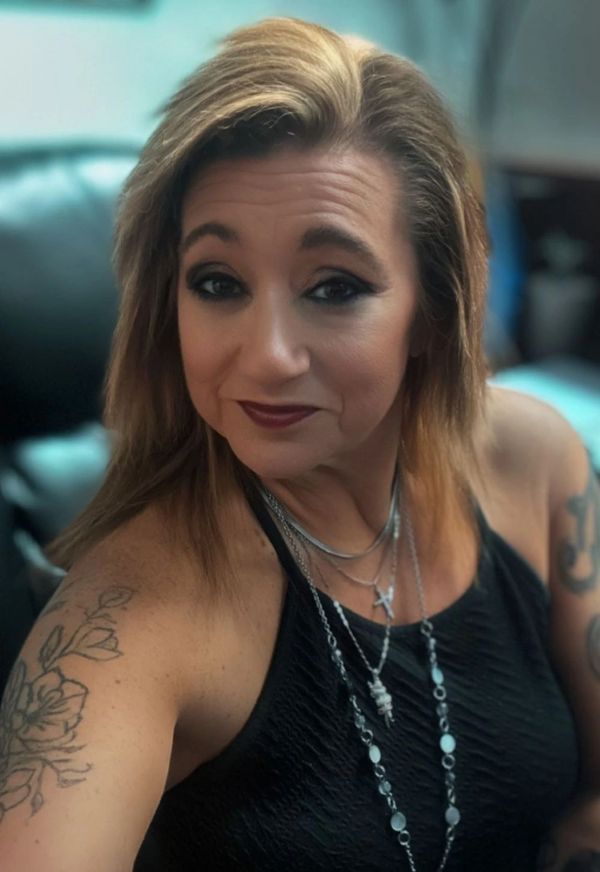 Woman with tattoos wearing layered necklaces and a black top.