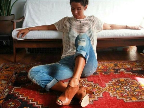 Person sitting cross-legged on a patterned carpet wearing blue jeans and brown heels.