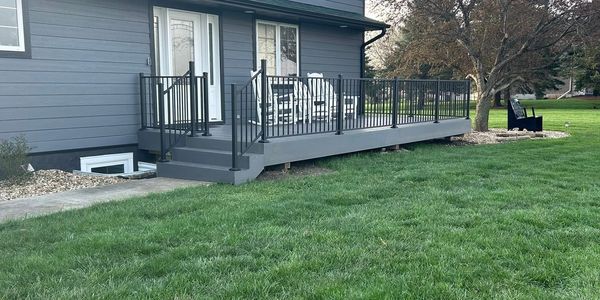 Modern wooden deck with black metal railing and white chairs.