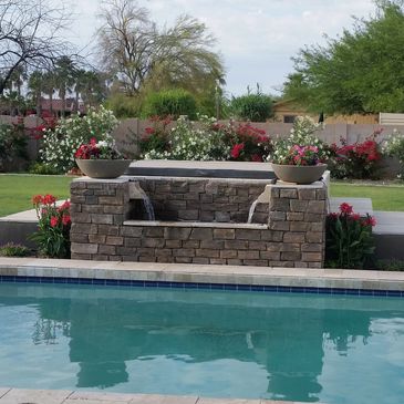 Stone water feature with planters by a backyard pool.