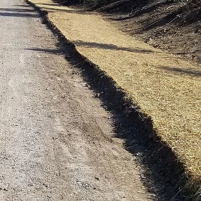 A rural gravel road with a field on one side and a straw-covered drainage ditch on the other.