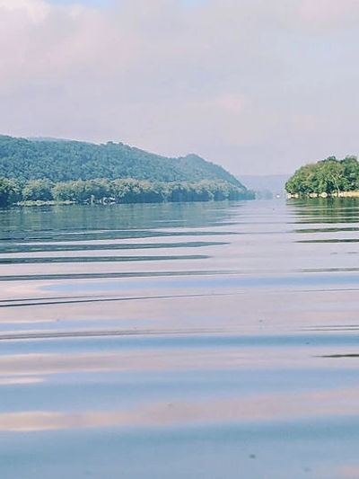 A calm river with small ripples, surrounded by lush, green hills and trees.