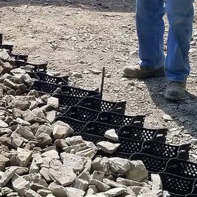 A worker stands next to a section of ground with a black honeycomb grid filled with gravel