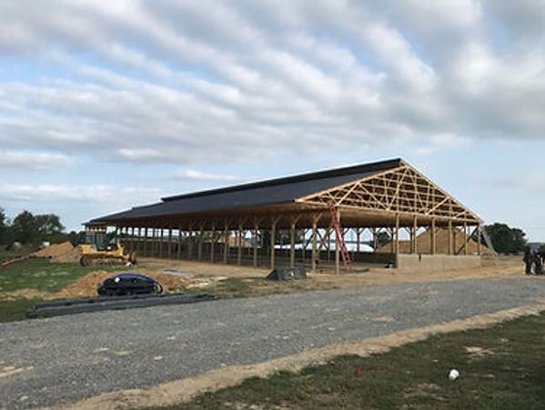 Partially constructed large wooden barn structure with an open frame under a cloudy sky.