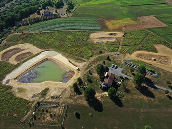 Aerial view of a farm with fields, ponds, buildings, and surrounding greenery.