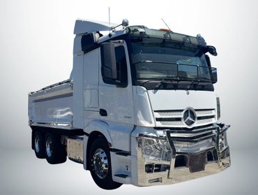 White Mercedes-Benz dump truck with chrome details and protective grille.