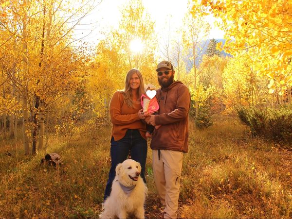 Family with a dog poses in a golden autumn forest, sun shining behind.